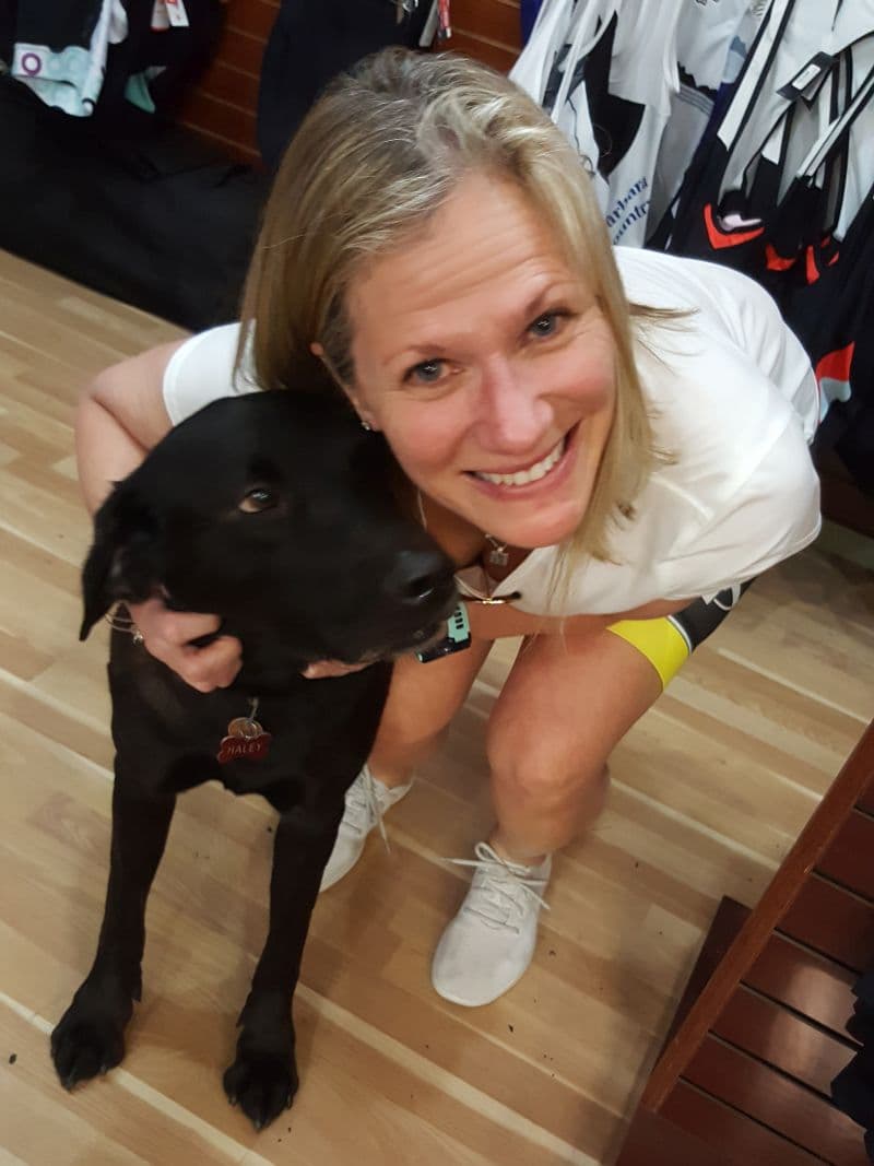 Suzy smiling beside a black dog indoors.